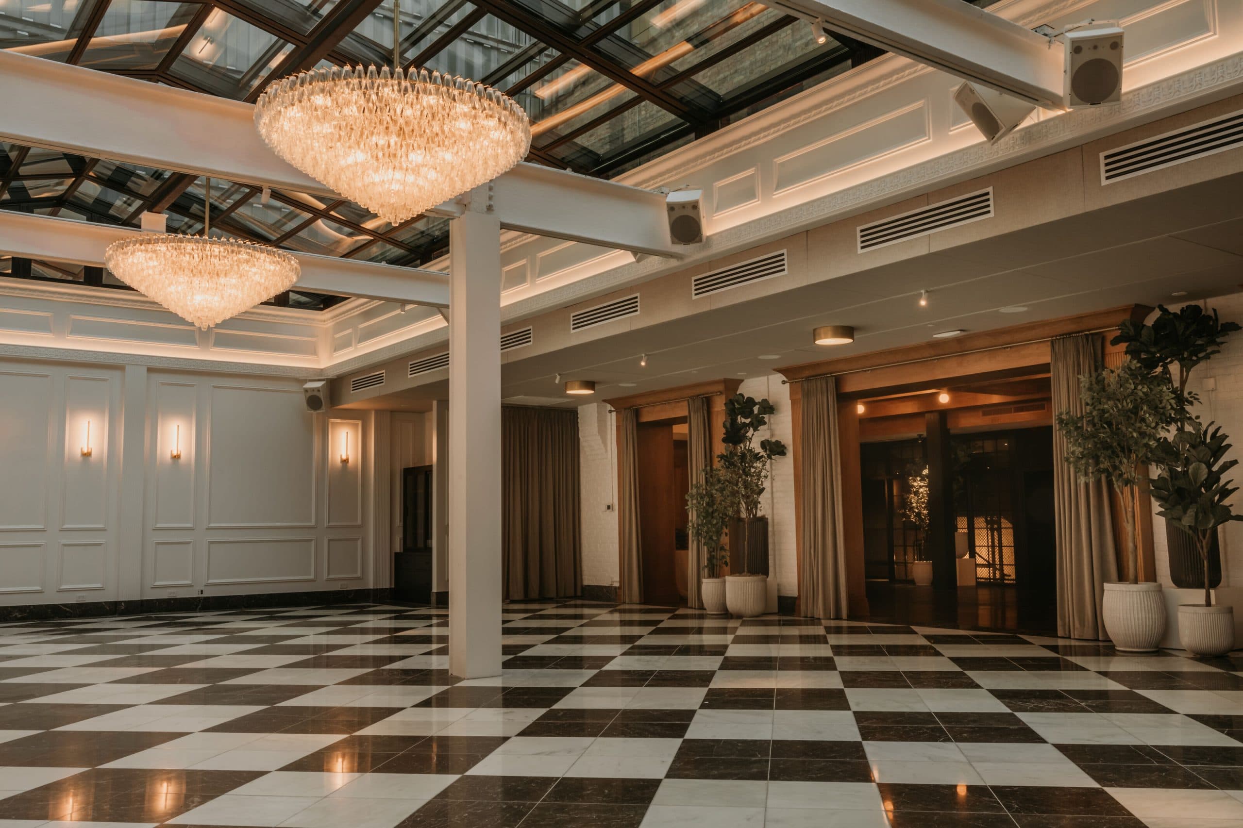 an open hall with a checkered floor and, plants, and circular chandeliers hang from the ceiling